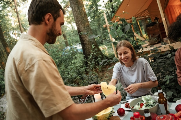 Young millennial woman with blonde hair smiling white teeth taking slice of watermelon from male friend. Summer full of vitamin, exotic fruit concept. Healthy diet, glamping food, unrefined sugar