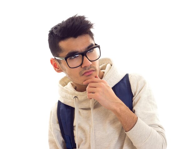 Young mirthless man with black hair in white hoody with black glasses and blue backpack in studio