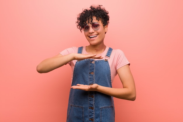 Young mixed african american teenager woman holding something with both hands, product presentation.