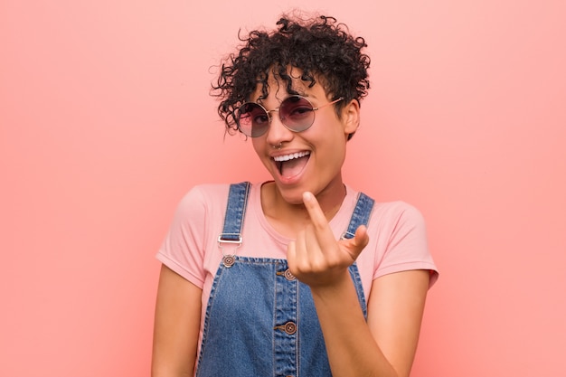 Young mixed african american teenager woman pointing with finger at you as if inviting come closer.