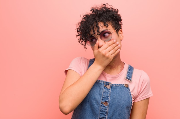 Young mixed african american teenager woman thoughtful looking to a copy space covering mouth with hand.