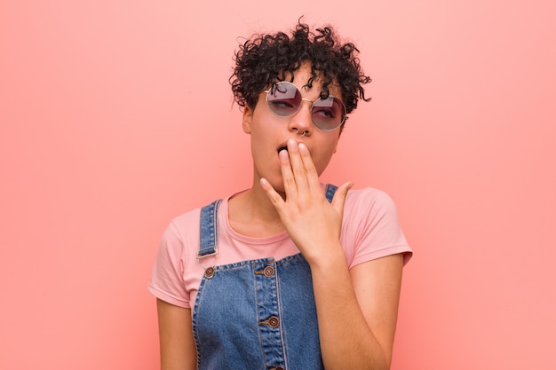 Young mixed african american teenager woman yawning showing a tired gesture covering mouth with hand.