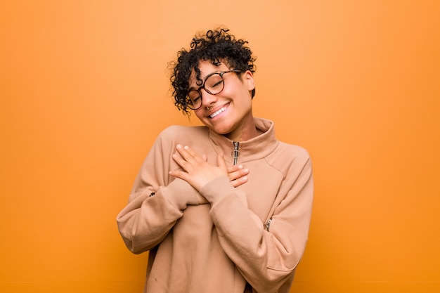 Young mixed african american woman against a brown background has friendly expression