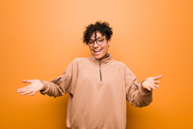 Young mixed african american woman against a brown background showing a welcome expression.