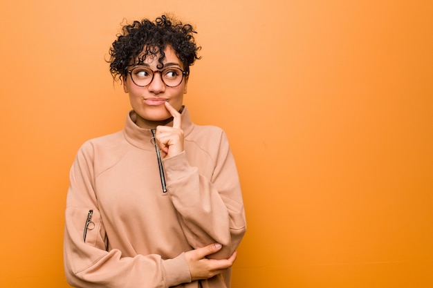 Young mixed african american woman against a brown wall looking sideways with doubtful and skeptical expression.