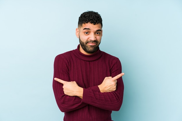 Young mixed race arabic man isolated points sideways, is trying to choose between two options.