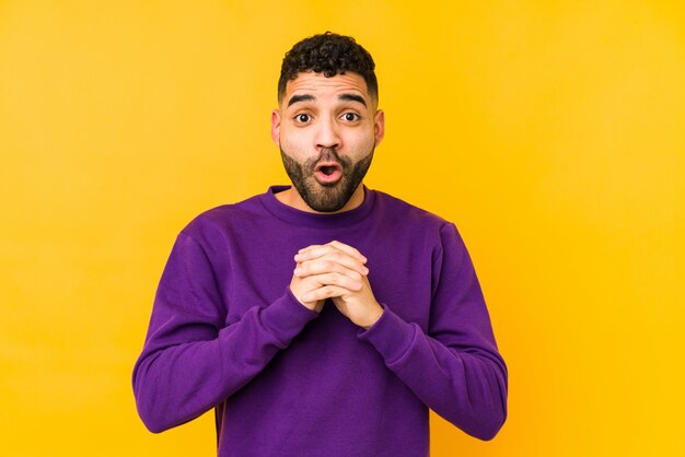 Young mixed race arabic man isolated praying for luck, amazed and opening mouth looking to front.