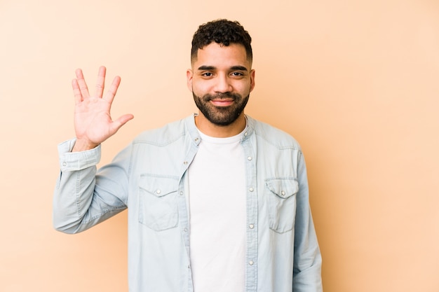 Young mixed race arabic man smiling cheerful showing number\
five with fingers.