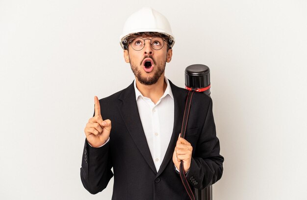 Young mixed race architect man wearing a helmet isolated on grey background pointing upside with opened mouth.