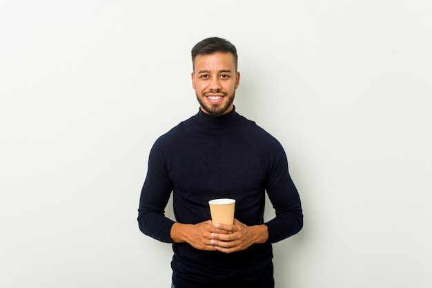 Young mixed race asian man holding a takeaway coffee happy, smiling and cheerful.