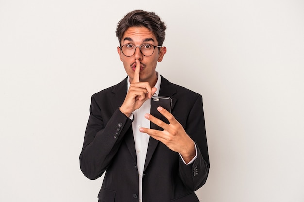 Young mixed race business man holding mobile phone isolated on white background keeping a secret or asking for silence.