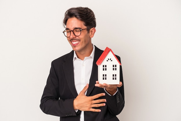 Young mixed race business man holding a toy house isolated on white background laughing and having fun.