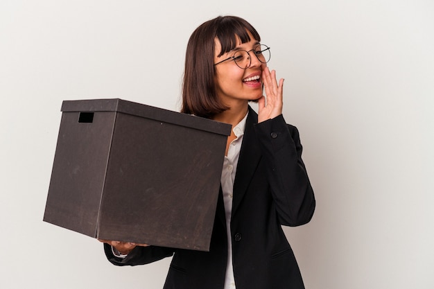 Young mixed race business woman holding a box isolated on white background shouting and holding palm near opened mouth.