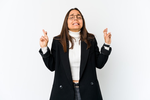 Young mixed race business woman isolated on white background crossing fingers for having luck