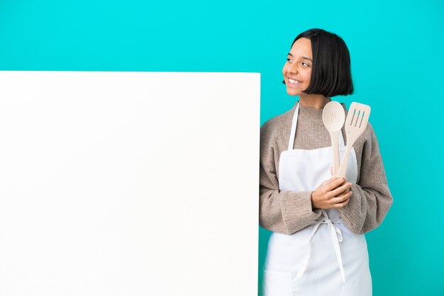 Young mixed race cook woman with a big placard isolated on blue background happy and smiling