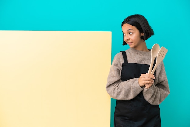 Young mixed race cook woman with a big placard isolated on blue background . Portrait