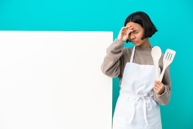 Young mixed race cook woman with a big placard isolated on blue background with tired and sick expression