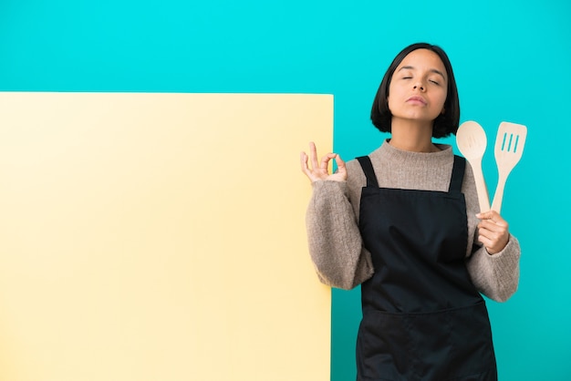 Young mixed race cook woman with a big placard isolated on blue wall in zen pose