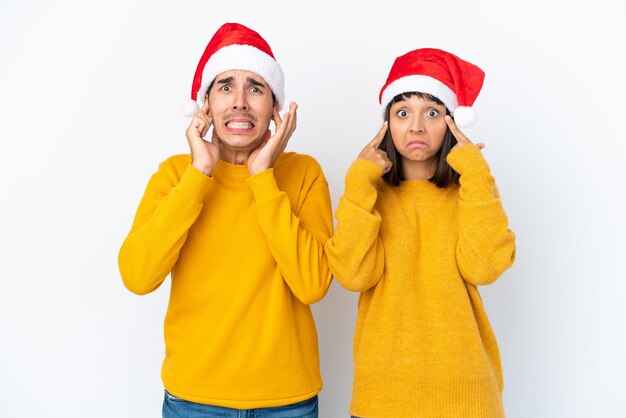 Foto giovane coppia di razza mista che celebra il natale isolato su sfondo bianco che copre entrambe le orecchie con le mani