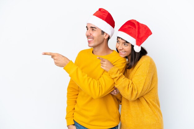 Giovane coppia di razza mista che celebra il natale isolato su sfondo bianco che punta al lato per presentare un prodotto