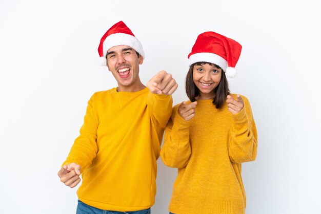 Young mixed race couple celebrating Christmas isolated on white background points finger at you while smiling