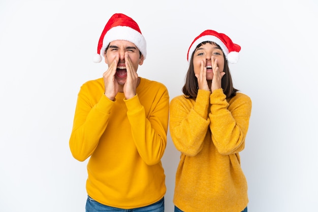 Young mixed race couple celebrating Christmas isolated on white background shouting and announcing something