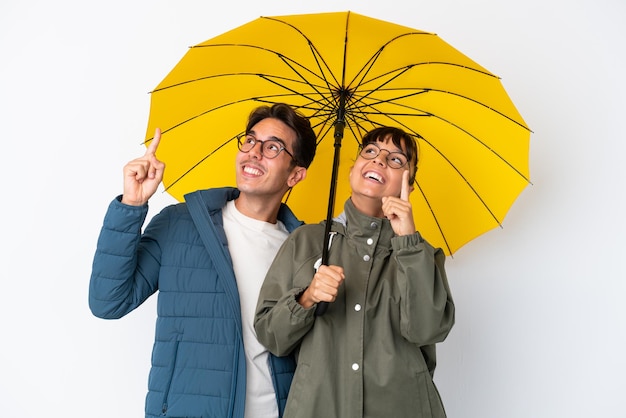 Young mixed race couple holding an umbrella isolated on white background pointing with the index finger a great idea