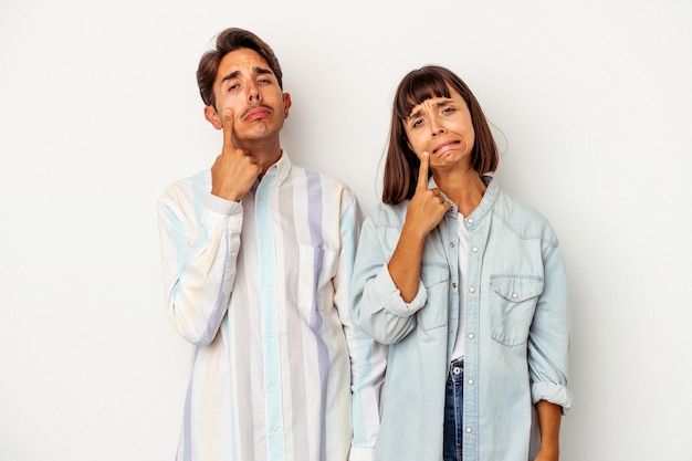 Young mixed race couple isolated on white background crying, unhappy with something, agony and confusion concept.