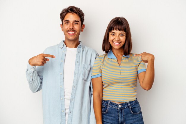 Young mixed race couple isolated on white background person pointing by hand to a shirt copy space, proud and confident