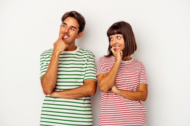 Young mixed race couple isolated on white background relaxed thinking about something looking at a copy space.