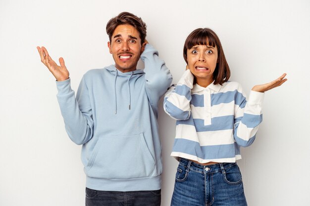 Young mixed race couple isolated on white background screaming with rage.