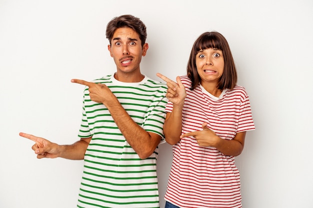 Photo young mixed race couple isolated on white background shocked pointing with index fingers to a copy space.