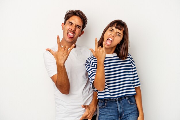 Young mixed race couple isolated on white background showing rock gesture with fingers