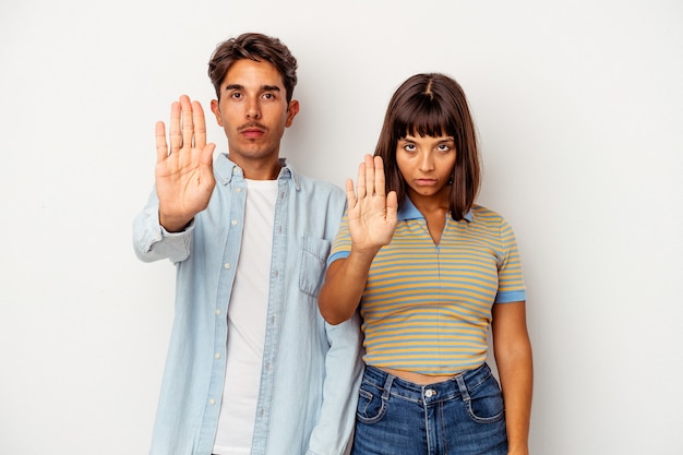 Young mixed race couple isolated on white background standing with outstretched hand showing stop sign, preventing you.