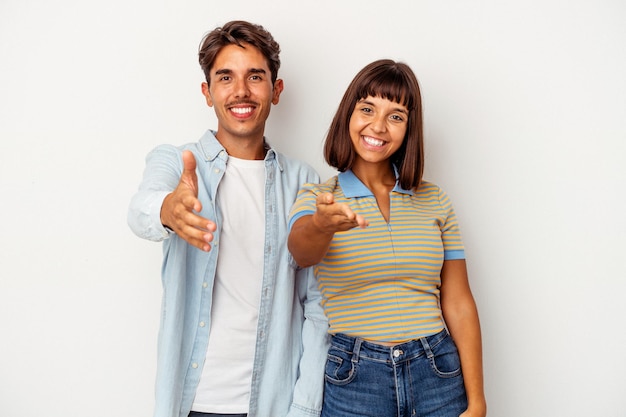 Young mixed race couple isolated on white background stretching hand at camera in greeting gesture.