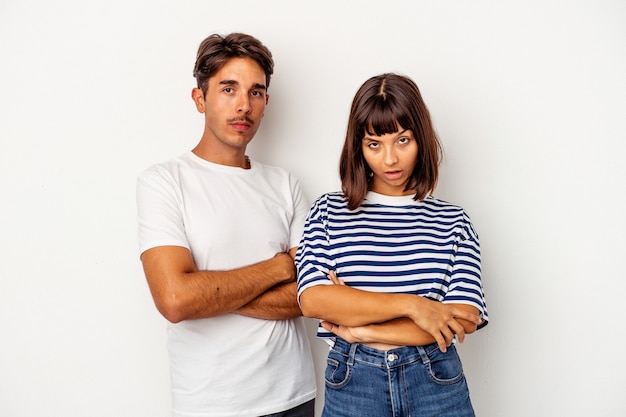 Young mixed race couple isolated on white background suspicious, uncertain, examining you.