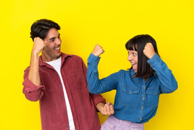 Young mixed race couple isolated on yellow background celebrating a victory in winner position