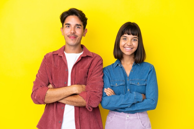 Young mixed race couple isolated on yellow background keeping the arms crossed in frontal position