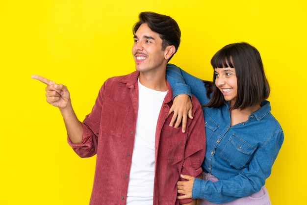 Young mixed race couple isolated on yellow background pointing to the side to present a product