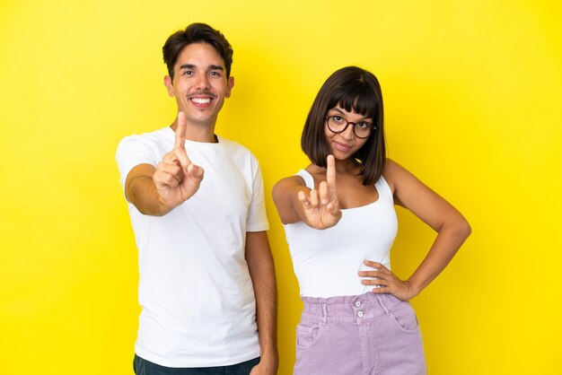 Young mixed race couple isolated on yellow background showing and lifting a finger