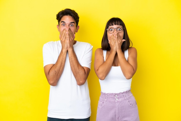 Young mixed race couple isolated on yellow background smiling a lot while covering mouth