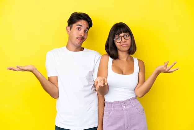 Young mixed race couple isolated on yellow background unhappy and frustrated with something because not understand something