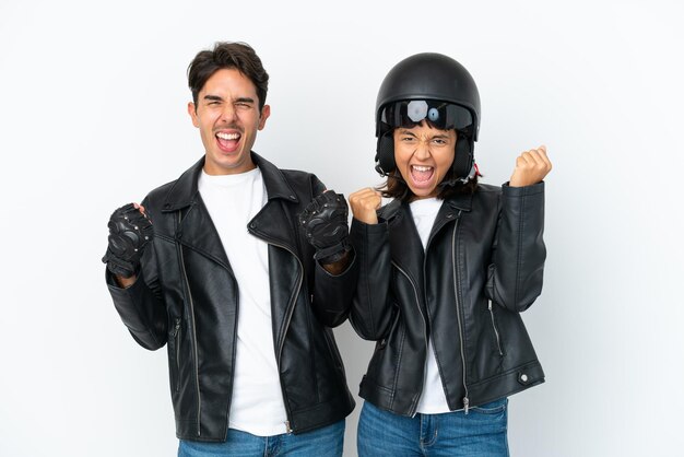 Foto giovane coppia di razza mista con un casco da motociclista isolato su sfondo bianco che celebra una vittoria