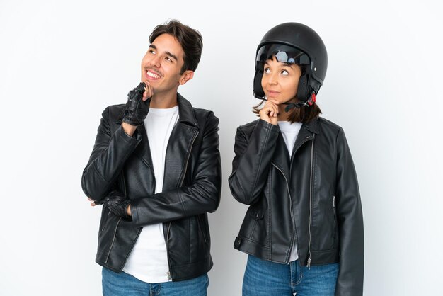 Young mixed race couple with a motorcycle helmet isolated on white background thinking an idea while looking up