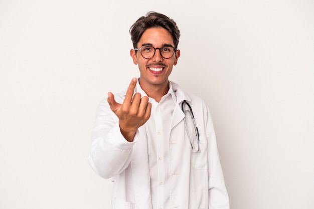 Young mixed race doctor man isolated on white background pointing with finger at you as if inviting come closer.