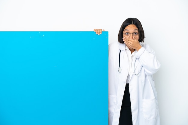Молодая женщина-врач смешанной расы с большим плакатом, изолированным на белом фоне, прикрывая рот руками