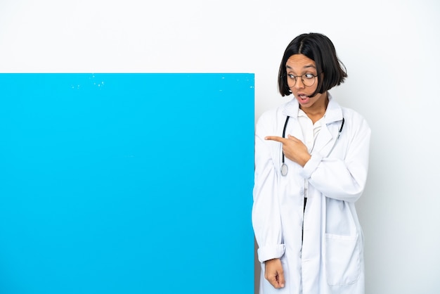 Young mixed race doctor woman with a big placard isolated on white background surprised and pointing side