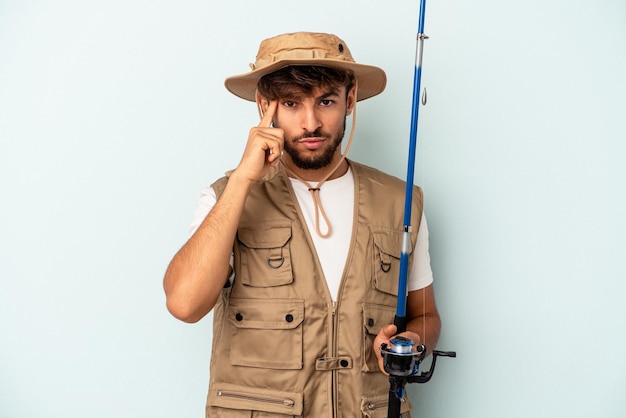 Young mixed race fisherman holding a rod isolated on blue background pointing temple with finger, thinking, focused on a task.