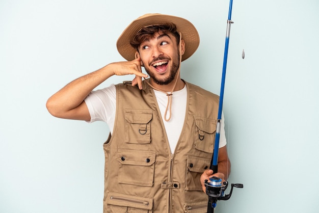 Young mixed race fisherman holding a rod isolated on blue background showing a mobile phone call gesture with fingers.