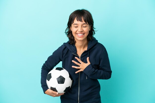 Young mixed race football player woman isolated on blue background smiling a lot